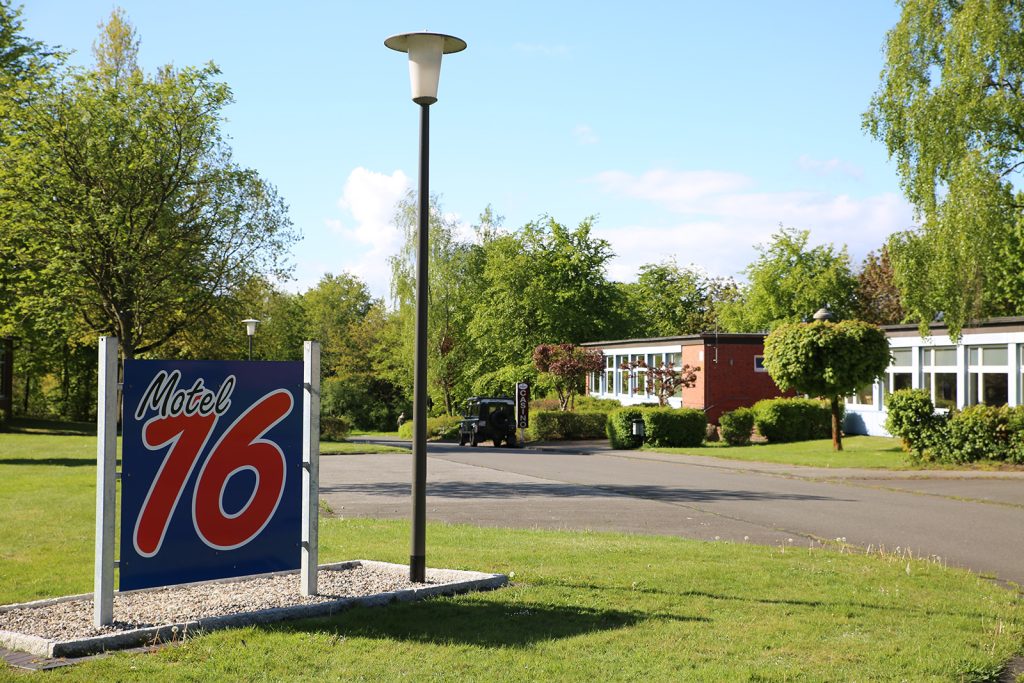 Firmenschild „Motel 16“ im Gewerbepark Albersdorf, umgeben von viel Grün; im Hintergrund ein Gebäude mit Büronutzung – ruhige Lage mit parkähnlicher Umgebung.